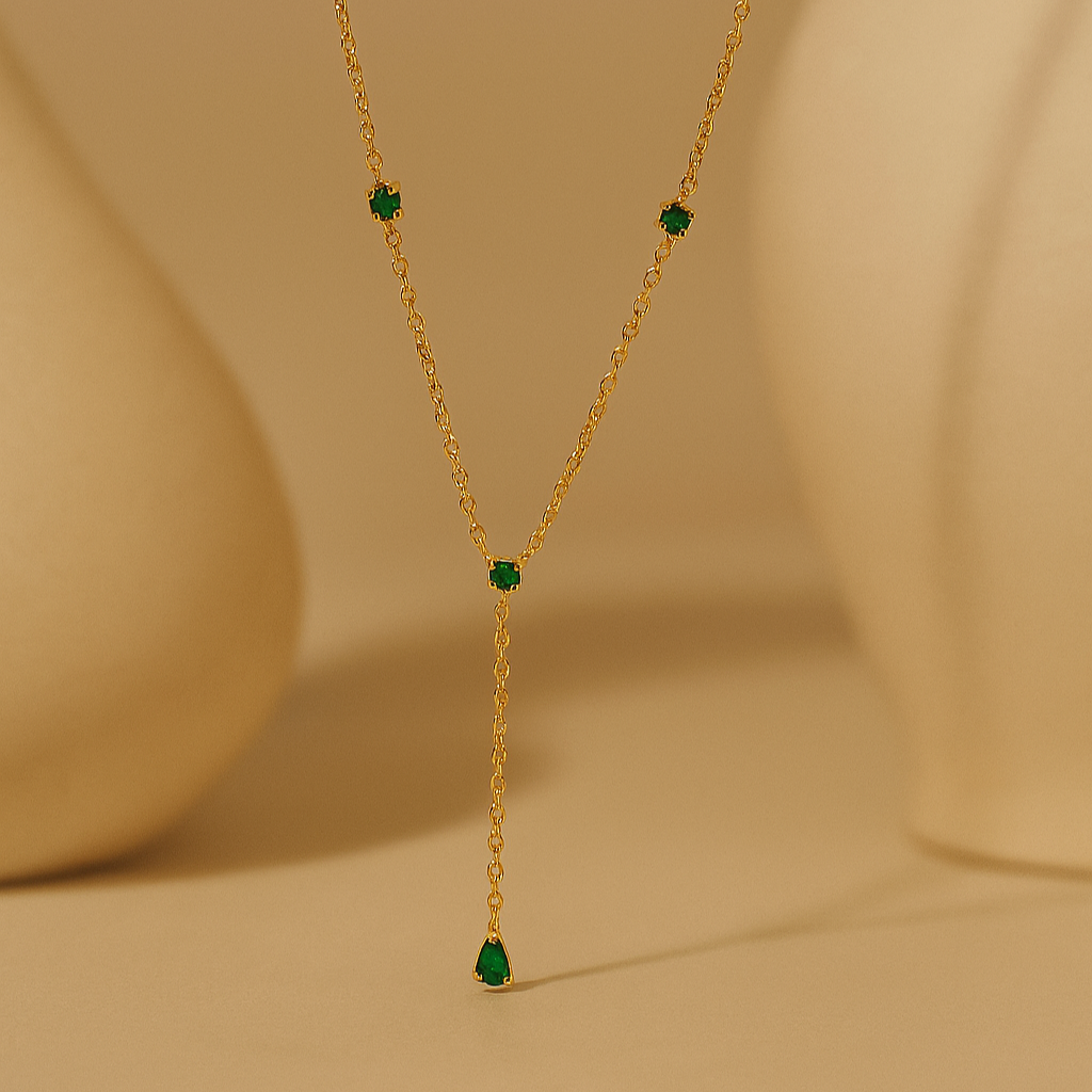 Gold necklace with green gemstones on a beige background