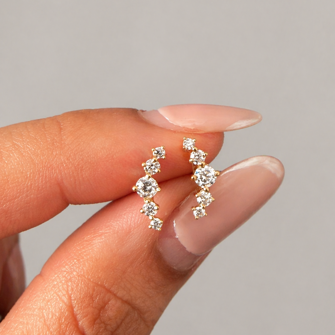 Gold and diamond earrings held between fingers against a neutral background