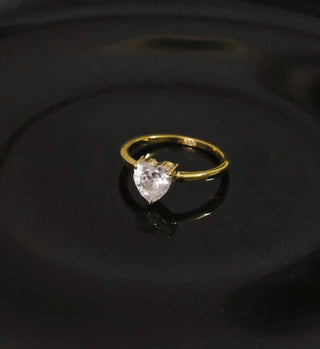 a gold ring with a white diamond on a black surface