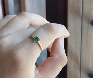 a woman's hand holding a ring with a green stone